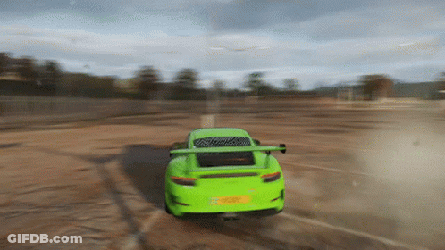 A Green Sports Car Is Driving On A Dirt Road . GIF