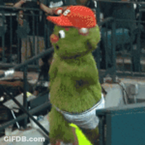 A Green Stuffed Animal Wearing A Red Hat And Diapers GIF