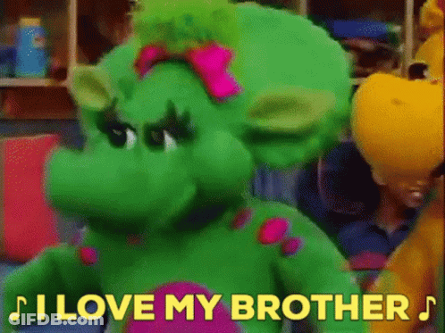 A Green Stuffed Animal With A Pink Bow On Its Head Is Standing Next To A Yellow Stuffed Animal . GIF