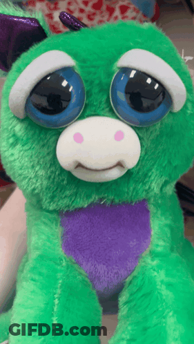 A Green Stuffed Animal With Blue Eyes And A Purple Heart On Its Chest GIF
