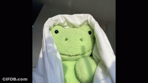 A Green Stuffed Frog Is Hiding Under A White Blanket . GIF