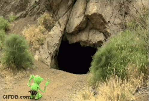 A Green Toy Is Standing In Front Of A Cave Entrance GIF