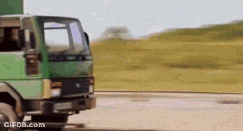 A Green Truck Is Driving Down A Dirt Road In A Field . GIF