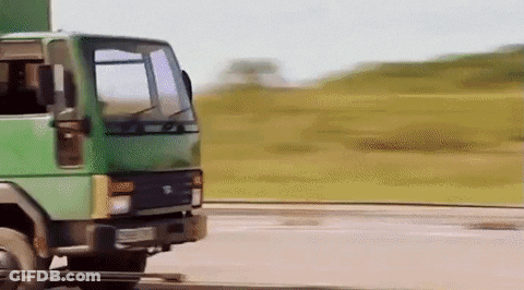 A Green Truck Is Driving Down A Road With Grass In The Background GIF