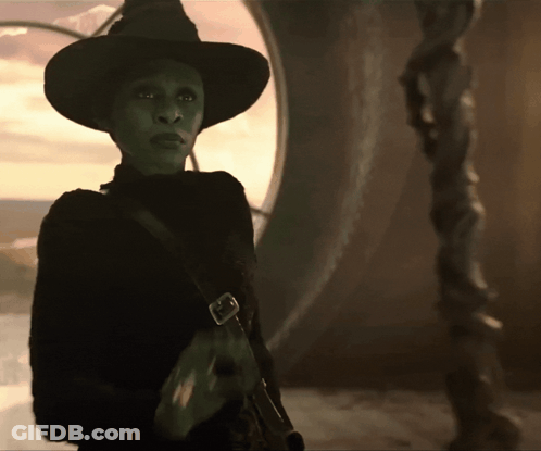 A Green Witch With A Black Hat And A Black Sweater GIF