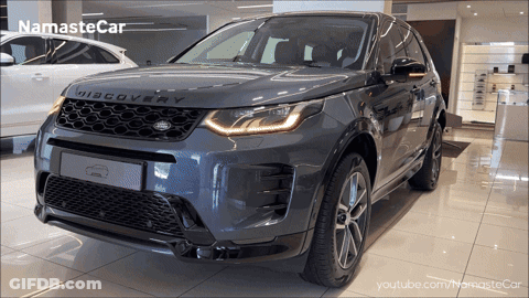 A Grey Land Rover Discovery Is Shown In A Showroom GIF