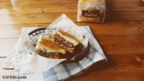 A Grilled Cheese Sandwich In A Basket On A Table Next To A Bag Of Nature 'S Own Bread GIF