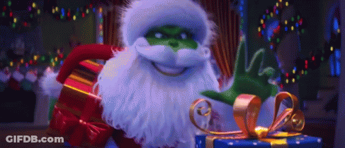 A Grinch Is Holding A Christmas Present And Waving At The Camera . GIF