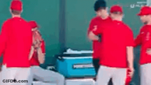 A Group Of Baseball Players Are Standing Around A Blue Cooler On The Field . GIF