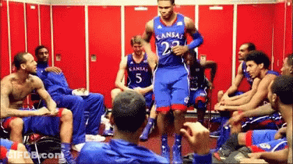 A Group Of Basketball Players Are Sitting In A Locker Room And One Has Kansas On His Jersey GIF