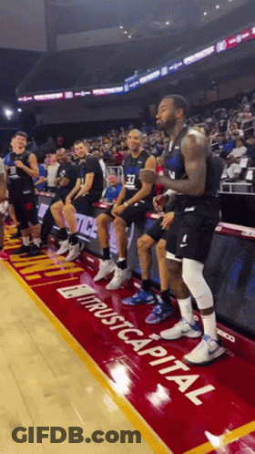 A Group Of Basketball Players Are Sitting On The Sidelines In Front Of A Sign That Says " Trust Capital " GIF