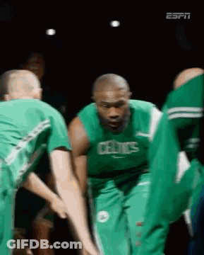A Group Of Basketball Players Wearing Green Uniforms Are Huddled Together . GIF