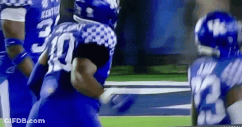 A Group Of Blue And White Football Players Are Playing A Game On A Field . GIF