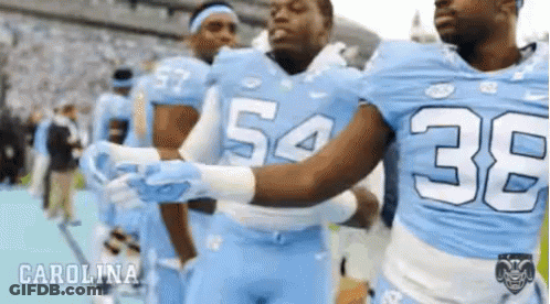 A Group Of Carolina Football Players Are Hugging Each Other On The Field GIF