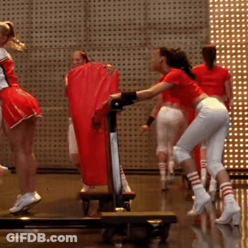 A Group Of Cheerleaders Are Standing On A Stage Holding A Red Bag GIF