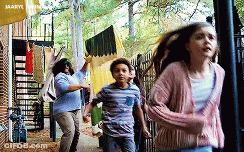 A Group Of Children Are Running Down A Sidewalk In Front Of A Building With Clothes Hanging On A Clothesline . GIF