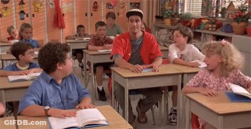 A Group Of Children Are Sitting At Their Desks In A Classroom With A Man In A Red Shirt Standing In The Middle . GIF