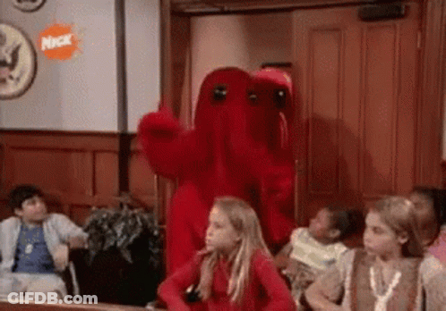 A Group Of Children Are Sitting In A Room With A Red Monster Mascot . GIF