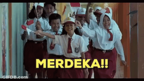 A Group Of Children In School Uniforms Are Walking Down A Hallway Holding Flags And A Sign That Says Merdeka . GIF