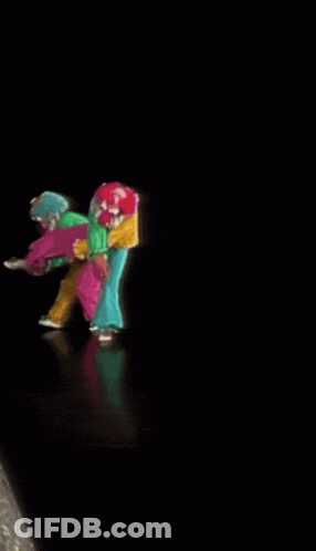 A Group Of Clowns Are Dancing On A Stage In A Dark Room GIF