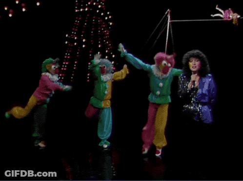 A Group Of Clowns Are Performing On Stage With A Woman Singing Into A Microphone GIF