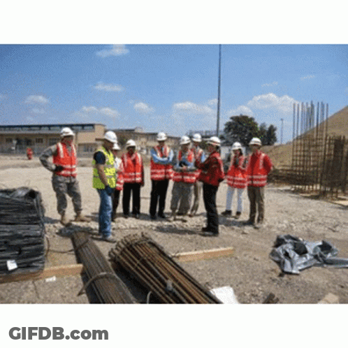 A Group Of Construction Workers Wearing Hard Hats Are Standing In A Dirt Field GIF