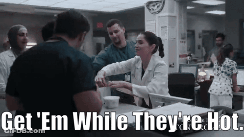 A Group Of Doctors And Nurses Are Standing Around A Counter With The Words Get ' Em While They 'Re Hot GIF