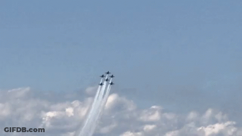 A Group Of Fighter Jets Flying Through A Blue Sky With Smoke Trails GIF