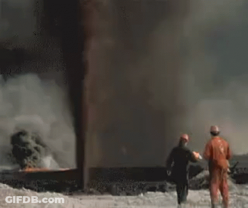 A Group Of Firefighters Are Standing In Front Of A Large Flame . GIF