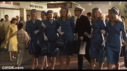 A Group Of Flight Attendants Are Walking In Front Of A Trans World Sign GIF