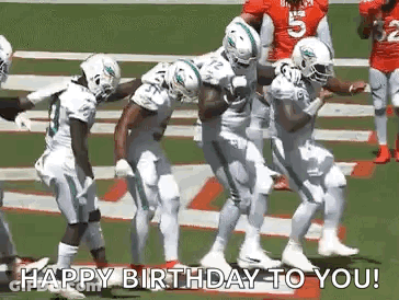 A Group Of Football Players Are Dancing On A Field While Holding A Football . GIF