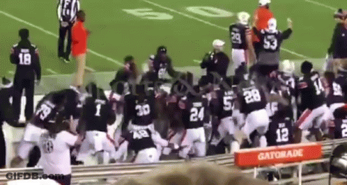 A Group Of Football Players Are Fighting On A Field In Front Of A Gatorade Stand . GIF
