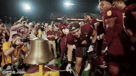 A Group Of Football Players Are Gathered Around A Bell GIF