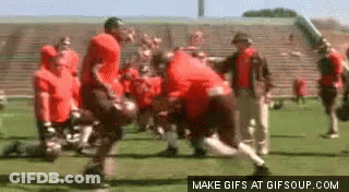 A Group Of Football Players Are Playing A Game On A Field In Front Of A Stadium . GIF