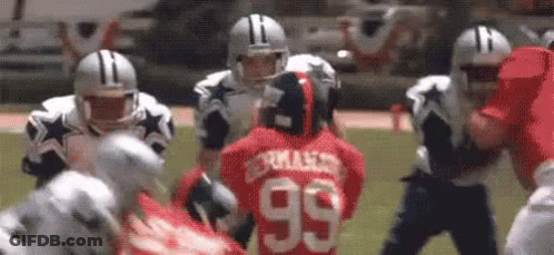 A Group Of Football Players Are Playing A Game On A Field . One Of The Players Has The Number 99 On His Jersey . GIF