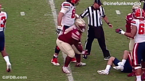 A Group Of Football Players Are Playing A Game On A Field With A Referee Standing Between Them . GIF