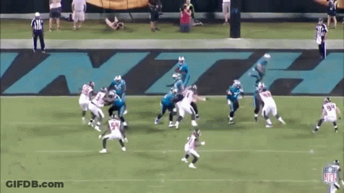 A Group Of Football Players Are Playing On A Field With A Large Nfl Logo Behind Them GIF