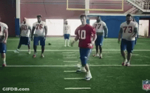 A Group Of Football Players Are Practicing On A Field In A Gym . GIF