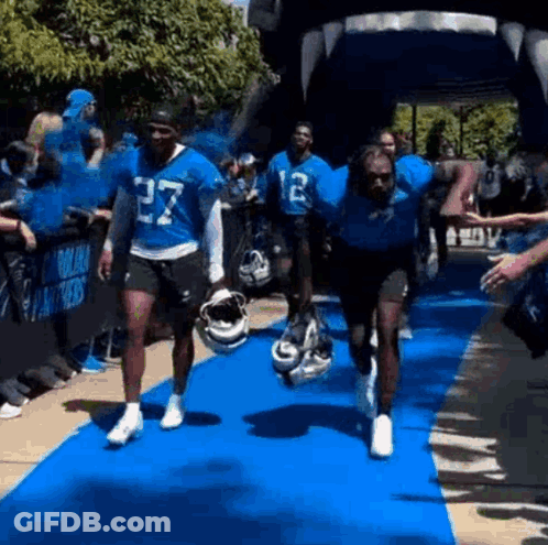 A Group Of Football Players Are Running On A Blue Carpet . GIF