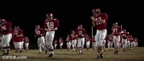 A Group Of Football Players Are Running On A Field At Night GIF