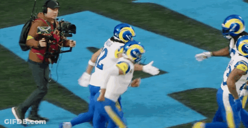 A Group Of Football Players Are Running On A Field While A Cameraman Takes A Picture Of Them . GIF