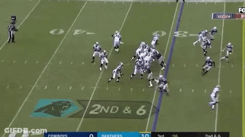 A Group Of Football Players Are Running On A Field While A Man Stands Behind Them . GIF