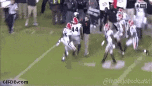 A Group Of Football Players Are Running On A Field While A Referee Watches . GIF