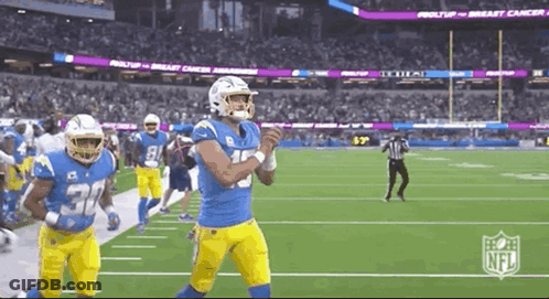 A Group Of Football Players Are Running On A Field With A Referee In The Background . GIF