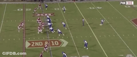 A Group Of Football Players Are Running On A Field With A Referee . GIF