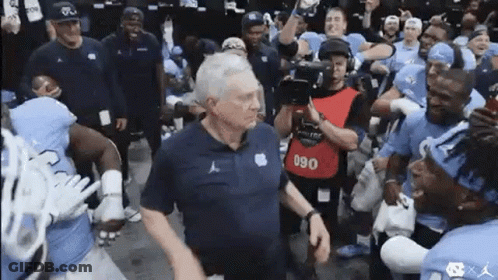 A Group Of Football Players Are Standing Around A Man . GIF