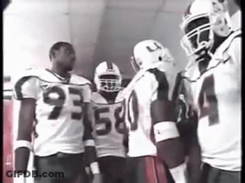 A Group Of Football Players Are Standing In A Hallway Talking To Each Other . GIF