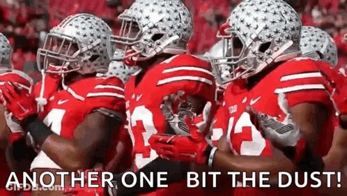 A Group Of Football Players Are Standing In A Line With The Words `` Another One Bit The Dust '' Written Above Them . GIF
