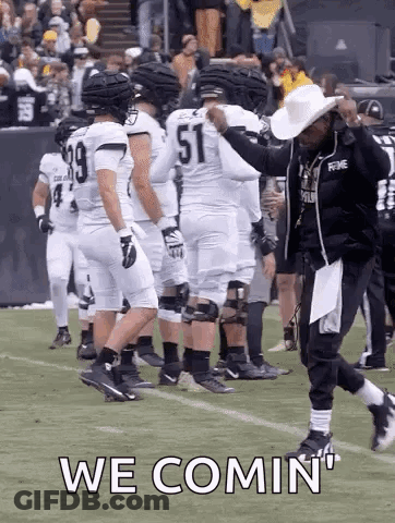 A Group Of Football Players Are Standing On A Field And A Man In A Cowboy Hat Is Walking On The Field . GIF