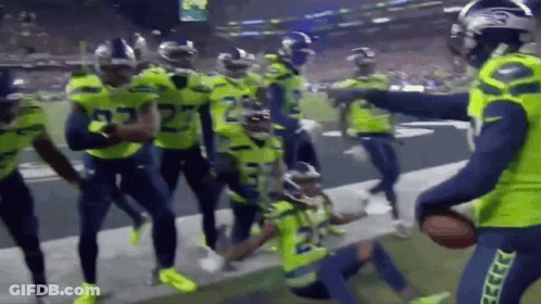 A Group Of Football Players Are Standing On A Field Holding A Ball . GIF